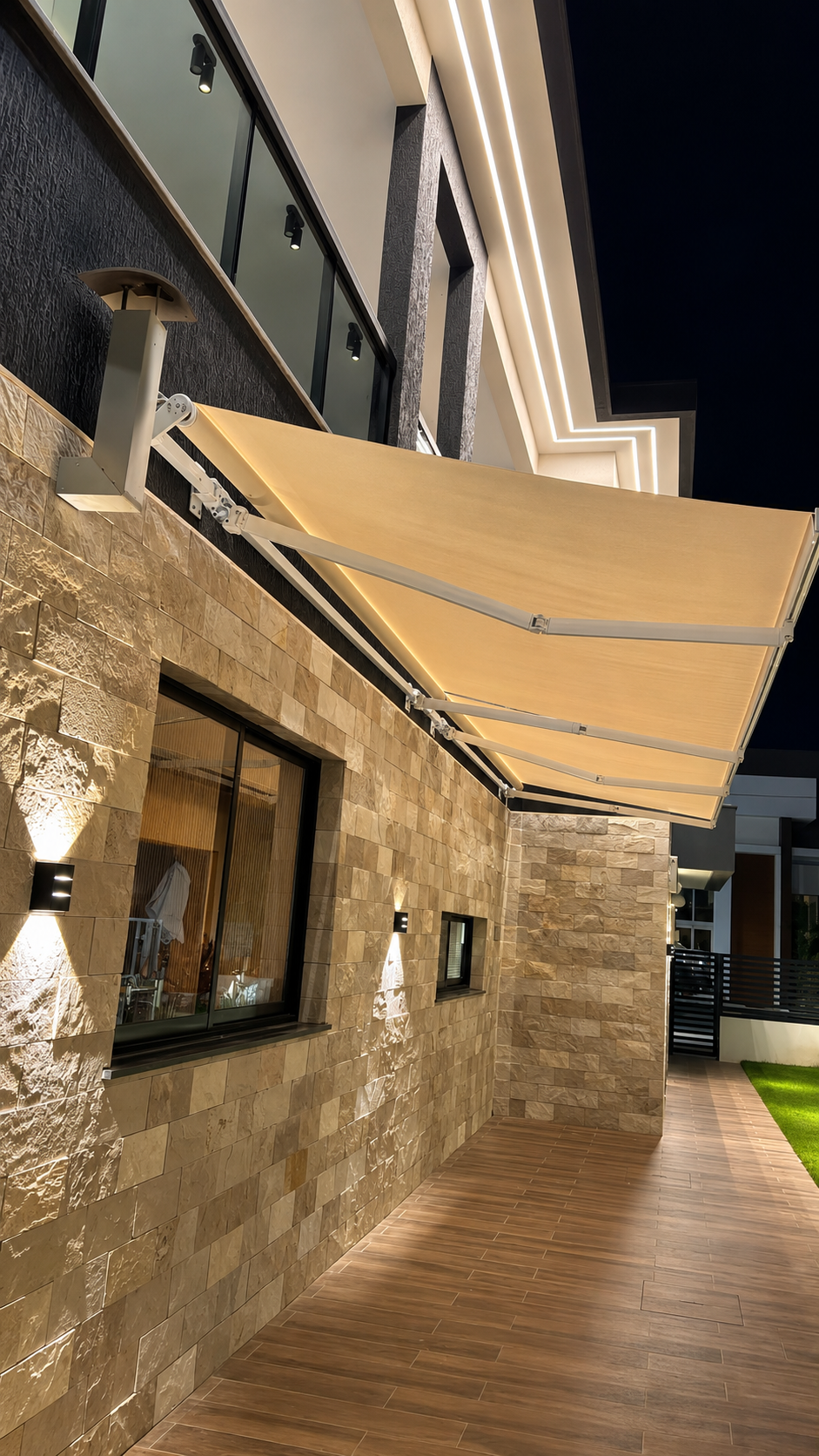 Toldo articulado em fachada residencial com iluminação noturna e revestimento em pedra
