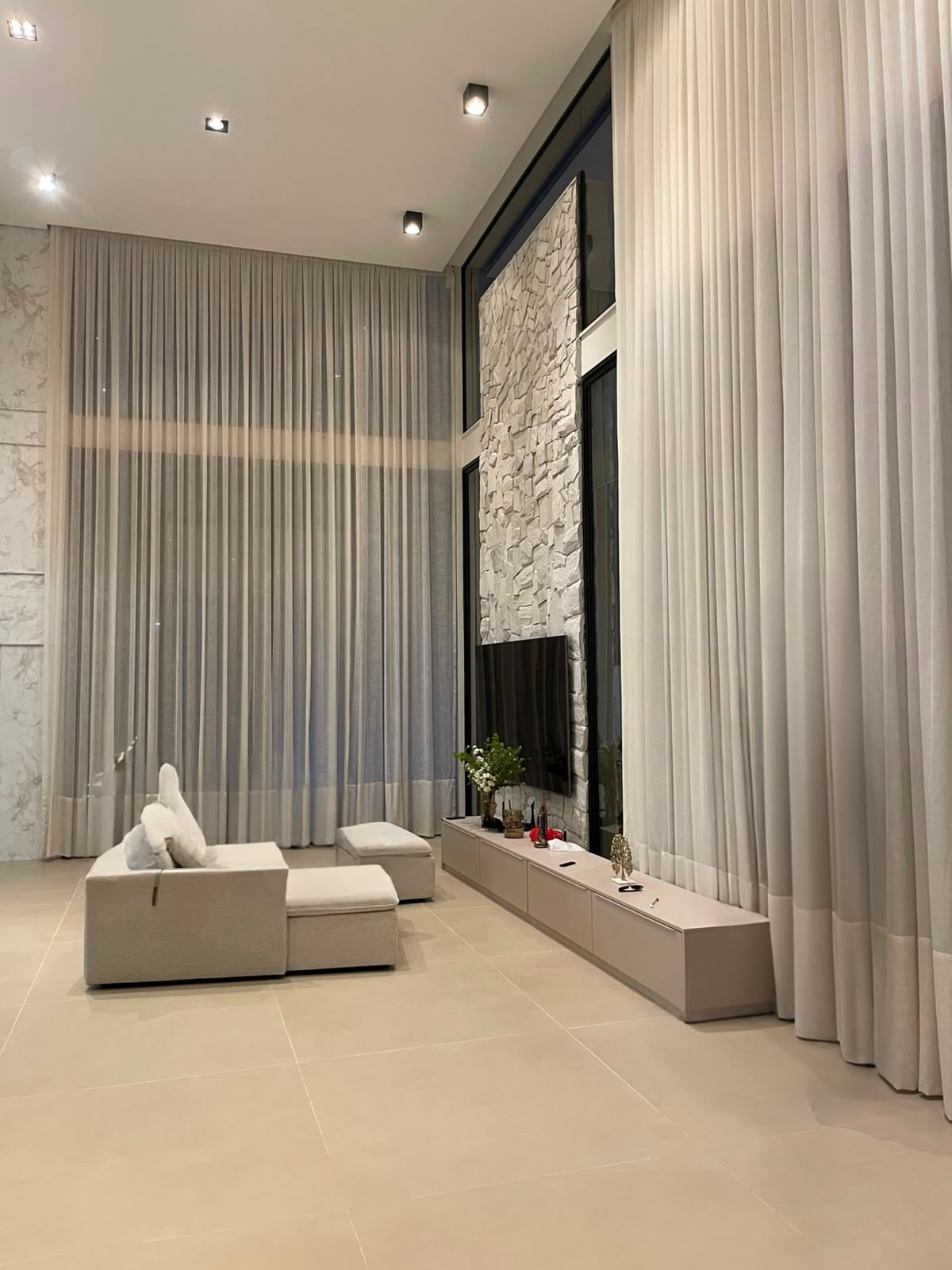 Cortinas de linho em sala de estar com pé-direito duplo e painel de pedra
