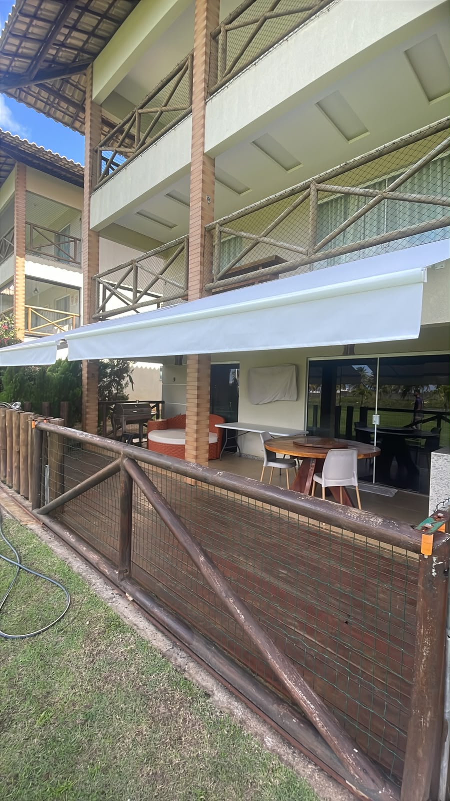 Toldo articulado branco instalado em varanda de resort com estrutura de madeira